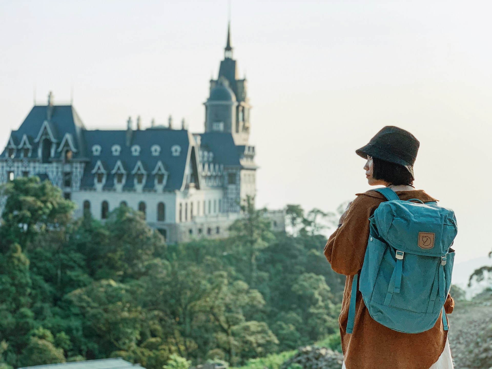 woman in blue denim jacket and black hat standing near white concrete building during daytime
